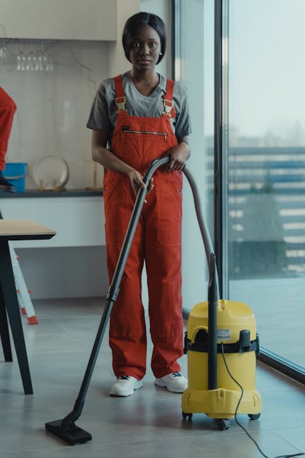 Three professional cleaning staff members from Cleaners Deep Cleaning standing indoors, each wearing grey shirts and bright orange aprons. The female on the left holds a vacuum cleaner hose, the male 